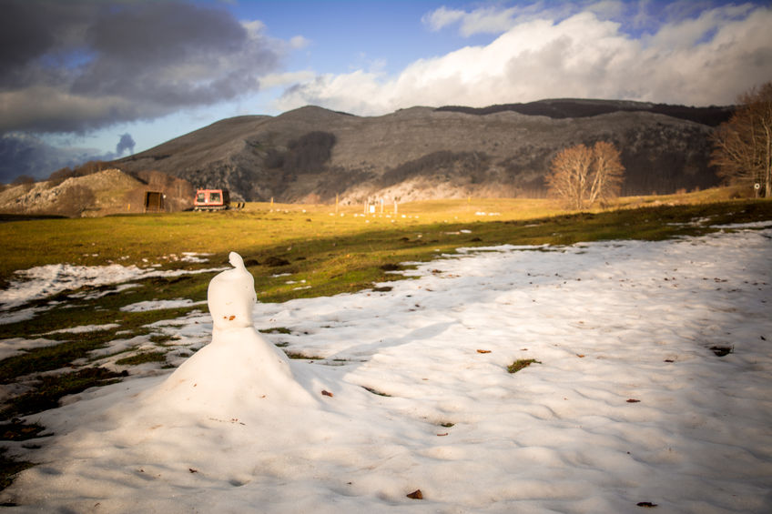 94242901 - horizontal view of a snowman that is melting during a hot day in spring on blur mountain landscape background